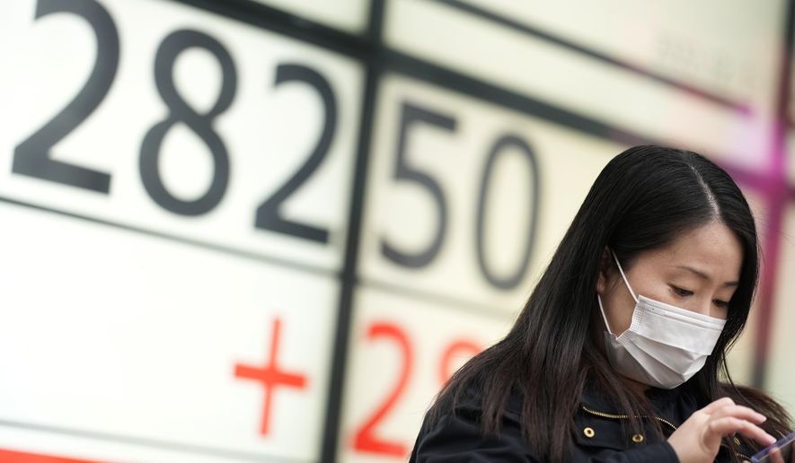 A woman uses her phone in front of monitors showing Japan&#39;s Nikkei 225 index at a securities firm while waiting for a traffic light in Tokyo, Thursday, Dec. 1, 2022. Shares have advanced in Asia after a rally on Wall Street spurred by the Federal Reserve chair&#39;s comments on easing the pace of interest rate hikes to tame inflation.(AP Photo/Hiro Komae)