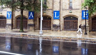 A woman walks by a Yale sign reflected in the rainwater in the street on the Yale University campus in New Haven, Conn., Aug. 22, 2021. (AP Photo/Ted Shaffrey, File)