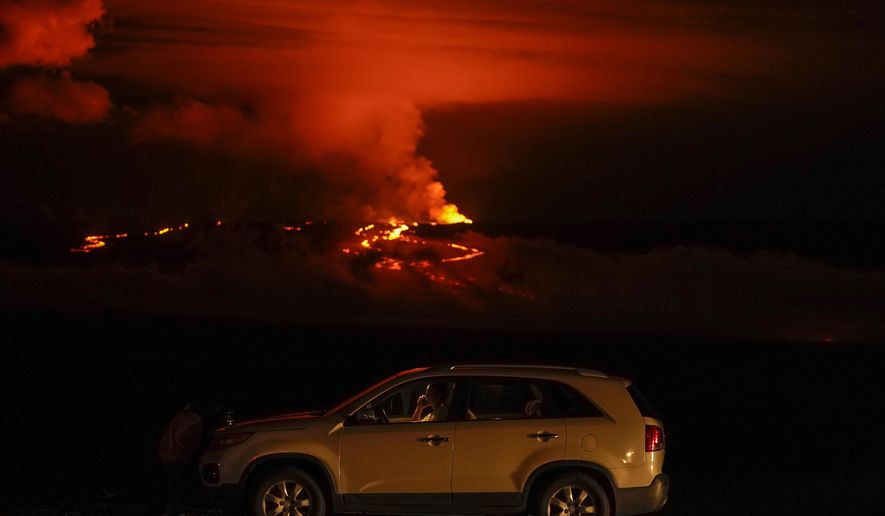 A man talks on a phone in his car alongside Saddle Road as the Mauna Loa volcano erupts Wednesday, Nov. 30, 2022, near Hilo, Hawaii. Hundreds of people in their cars lined Saddle Road, which connects the east and west sides of the island, as lava flowed down the side of Mauna Loa and could be seen fountaining into the air on Wednesday. (AP Photo/Gregory Bull)