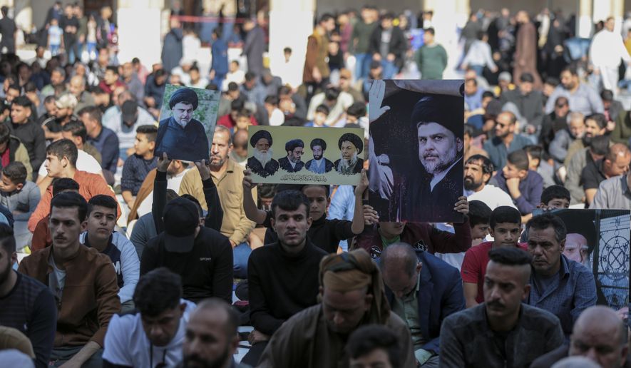 People hold up pictures of the Shiite cleric Muqtada al-Sadr during Friday prayers at a mosque in Kufa, Iraq, Friday, Dec. 2, 2022. Al-Sadr who announced his withdrawal from politics four months ago has broken a period of relative silence to launch an anti-LGBTQ campaign. (AP Photo/Anmar Khalil)