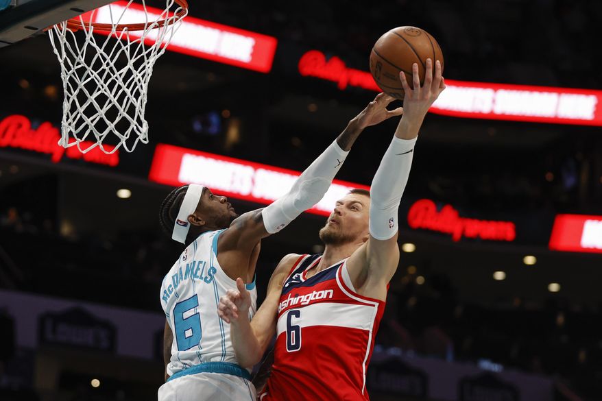 Washington Wizards center Kristaps Porzingis, right, shoots against Charlotte Hornets forward Jalen McDaniels during the first half of an NBA basketball game in Charlotte, N.C., Friday, Dec. 2, 2022. (AP Photo/Nell Redmond)