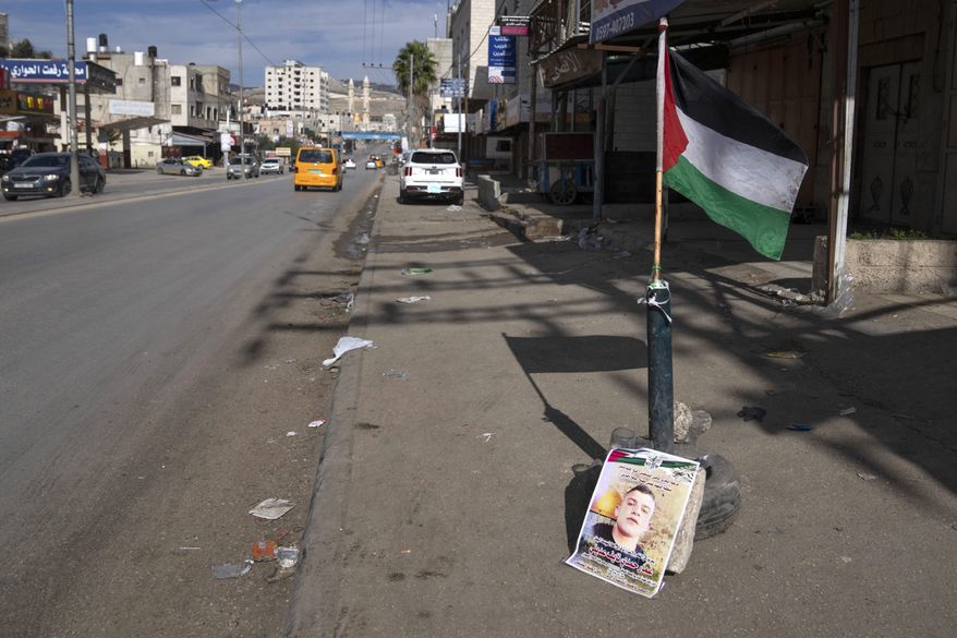 A Palestinian flag and a poster showing Ammar Adili, 22, who was shot and killed by an Israeli border police officer on Friday, mark the location of the incident, on the main thoroughfare where shops are closed in a general strike, in the West Bank town of Hawara, south of Nablus, Saturday, Dec. 3, 2022. Palestinians pushed back Saturday against Israeli police claims that Ammar Adili had attacked Israelis, including a border policeman, in the area and that he was shot in self-defense. They said the officer killed Adili without cause, and that Palestinian medics were kept from trying to save him as he lay gravely wounded on the side of a busy throughfare in the occupied West Bank town of Hawara.(AP Photo/Nasser Nasser)