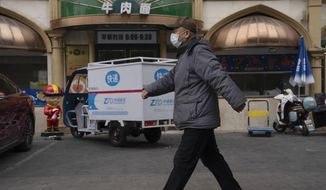 A man wearing a mask walks near a restaurant in Beijing, Friday, Dec. 2, 2022. More cities eased restrictions, allowing shopping malls, supermarkets and other businesses to reopen following protests last weekend in Shanghai and other areas in which some crowds called for President Xi Jinping to resign. (AP Photo/Ng Han Guan)