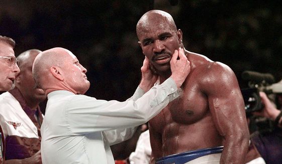 Evander Holyfield has his right ear checked by referee Mills Lane after he was bit on the ear by Mike Tyson during the third round of their WBA heavyweight boxing match June 28, 1997, in Las Vegas. Lane, the Hall of Fame boxing referee who was the third man in the ring when Tyson bit Holyfield’s ear, died Tuesday, Dec. 6, 2022. He was 85. Lane had suffered a stroke in 2002 and son Tommy said his father had taken a significant turn for the worse recently before entering hospice care Friday. (AP Photo/Mark J. Terrill, File) ** FILE**