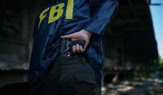 FBI agent holding a gun in his hand, rear view. File photo credit: Shutterstock