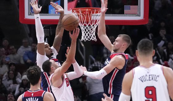 Chicago Bulls&#39; Zach LaVine shorts between Washington Wizards&#39; Daniel Gafford, left, and Kristaps Porzingis during the second half of an NBA basketball game Wednesday, Dec. 7, 2022, in Chicago. The Bulls won 115-111. (AP Photo/Charles Rex Arbogast)
