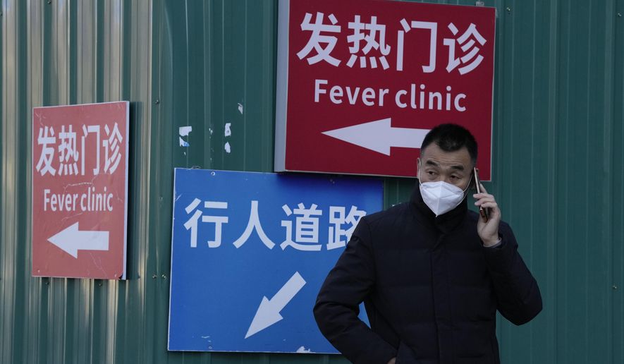 A man wearing a mask talks on his phone near signs directing visitors to the fever clinic at a hospital in Beijing, Saturday, Dec. 10, 2022. A rash of COVID-19 cases in schools and businesses were reported Friday in areas across China after the ruling Communist Party loosened anti-virus rules as it tries to reverse a deepening economic slump. (AP Photo/Ng Han Guan)