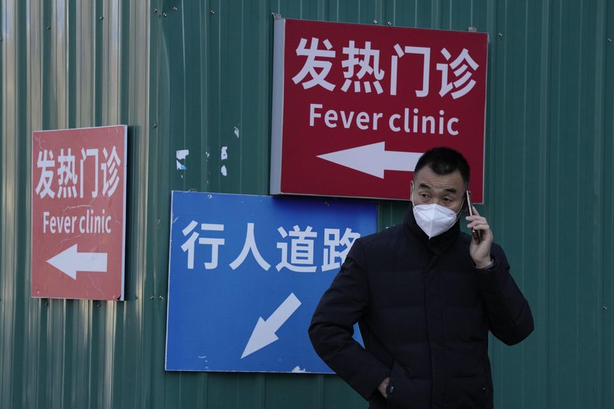 A man wearing a mask talks on his phone near signs directing visitors to the fever clinic at a hospital in Beijing, Saturday, Dec. 10, 2022. A rash of COVID-19 cases in schools and businesses were reported Friday in areas across China after the ruling Communist Party loosened anti-virus rules as it tries to reverse a deepening economic slump. (AP Photo/Ng Han Guan)