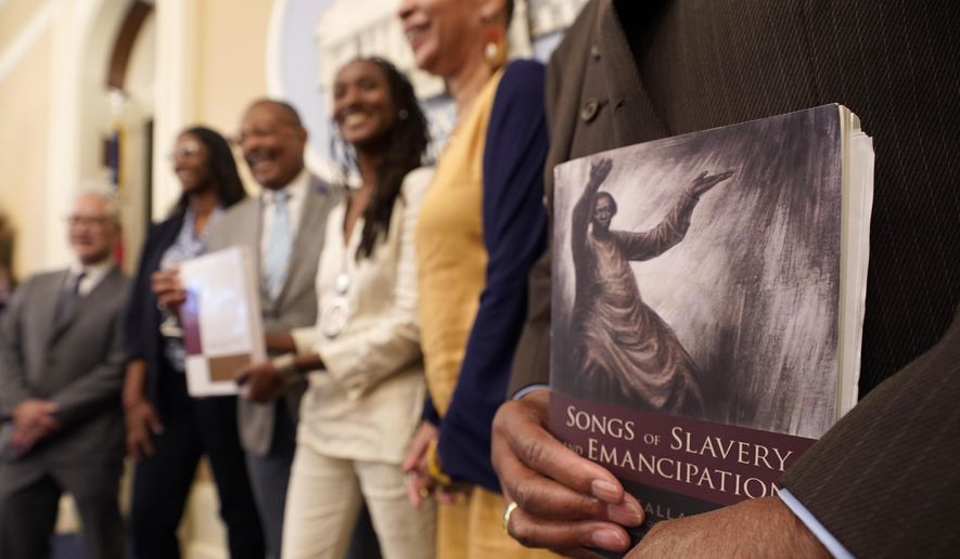 Dr. Amos C. Brown, Jr., vice chair for the California Reparations Task Force, right, holds a copy of the book Songs of Slavery and Emancipation, as he and other members of the task force pose for photos at the Capitol in Sacramento, Calif., on June 16, 2022. California&#x27;s committee to study reparations for African Americans will meet in Oakland Wednesday, Dec. 14, 2022, to discuss requirements for residents who may receive some form of compensation. (AP Photo/Rich Pedroncelli, File)