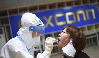 A medical worker takes a swab sample to test for COVID-19 from a worker at the Foxconn factory in Wuhan in central China&#x27;s Hubei province Thursday, Aug. 5, 2021. Foxconn, the company that assembles Apple Inc.’s iPhones, has announced it is easing COVID-19 restrictions at its largest factory, in Zhengzhou, central China, that led thousands of workers to quit and drastically slowed production. (Chinatopix Via AP, File)