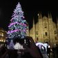 A woman takes pictures of a lit Christmas tree in front of the Duomo gothic cathedral in Milan, Italy, Friday, Dec. 16, 2022. (AP Photo/Antonio Calanni)