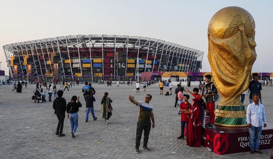 People pose for pictures next to a replica of the World Cup Trophy, right, with the Stadium 974 in the background before the Qatar Fashion United event in Doha, Qatar, Friday, Dec. 16, 2022. (AP Photo/Pavel Golovkin)