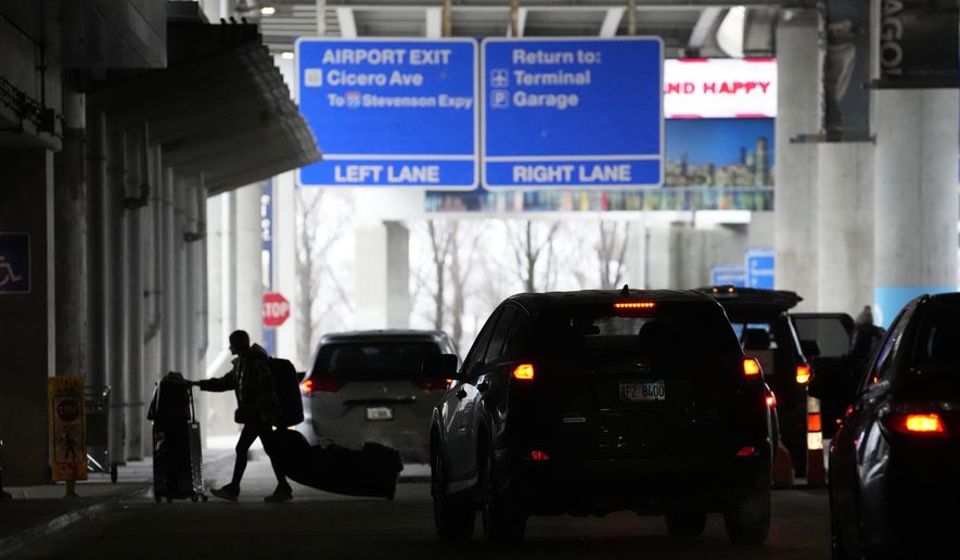 An airline passenger walks between ride share vehicles after arriving at Chicago&#x27;s Midway Airport just days before a major winter storm Tuesday, Dec. 20, 2022, in Chicago. (AP Photo/Charles Rex Arbogast)
