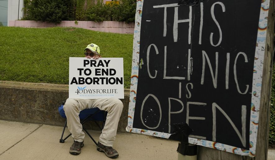 FILE -  An anti-abortion supporter sits behind a sign that advises the Jackson Women&#x27;s Health Organization clinic is still open in Jackson, Miss., Wednesday, July 6, 2022. (AP Photo/Rogelio V. Solis, File)