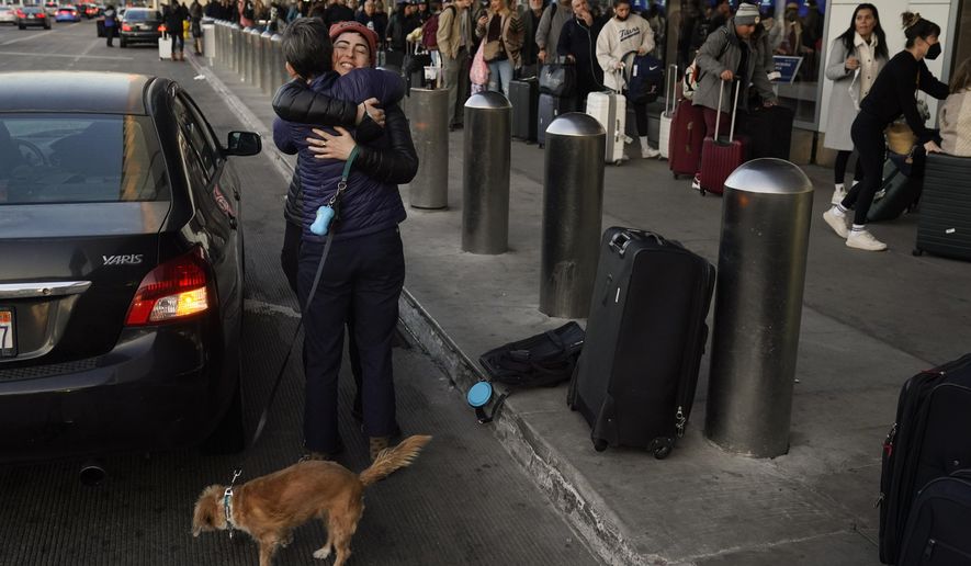 Two people hug outside a terminal as travelers wait in line to check in at Los Angeles International Airport in Los Angeles, Monday, Dec. 19, 2022. (AP Photo/Jae C. Hong)