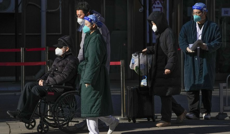 Medical workers in protective gear escort an elderly patient on a wheelchair followed by family members as they leave a fever clinic at a hospital in Beijing on Monday, Dec. 19, 2022. A Chinese health official said that the country would only count those who died from pneumonia or respiratory failure in the official COVID death toll, a narrow definition that would certainly limit the numbers of deaths reported, as the country's reopening progresses and cases have soared. (AP Photo/Andy Wong)
