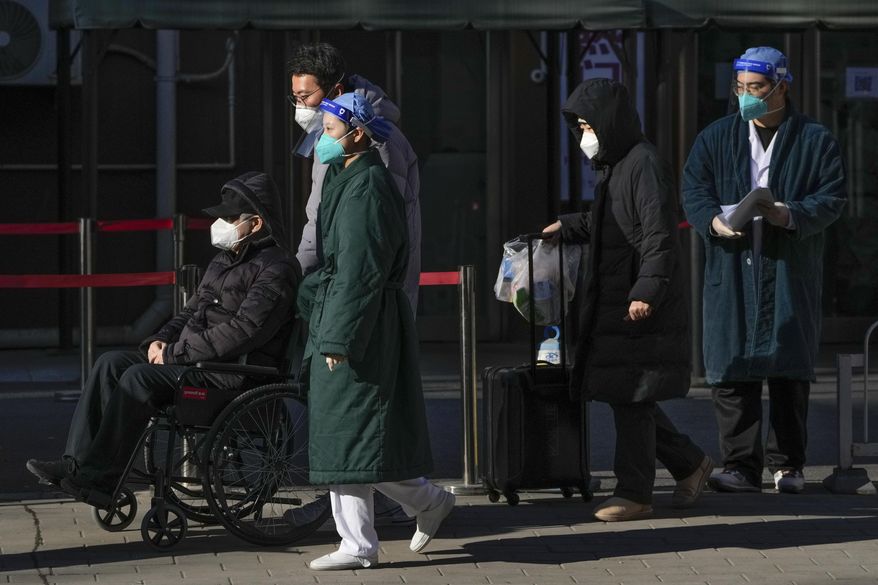 Medical workers in protective gear escort an elderly patient on a wheelchair followed by family members as they leave a fever clinic at a hospital in Beijing on Monday, Dec. 19, 2022. A Chinese health official said that the country would only count those who died from pneumonia or respiratory failure in the official COVID death toll, a narrow definition that would certainly limit the numbers of deaths reported, as the country's reopening progresses and cases have soared. (AP Photo/Andy Wong)