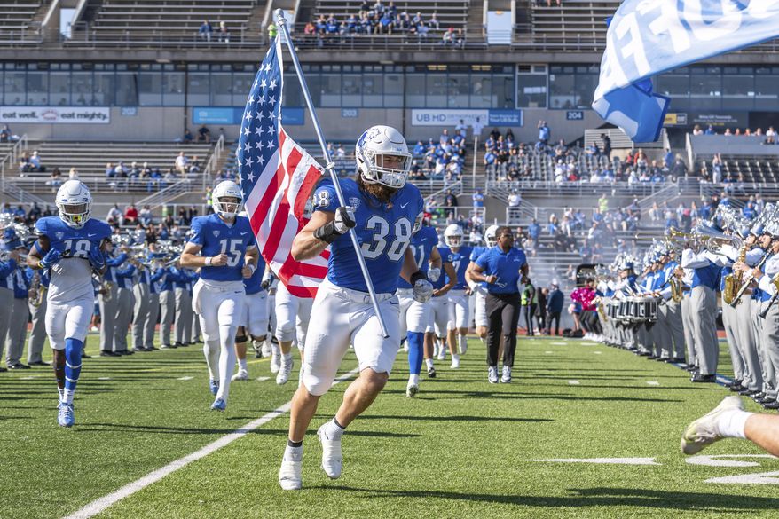 This Oct. 22, 2022, photo provided by University of Buffalo Athletics shows University at Buffalo NCAA college football player Damian Jackson (38) carrying the American flag as the team takes the field before a game against Toledo, in Buffalo, N.Y. Jackson has no expectation of growing emotional in preparing to play the final game of his college career next week. (Paul Hokanson/Univ. of Buffalo Athletics via AP)