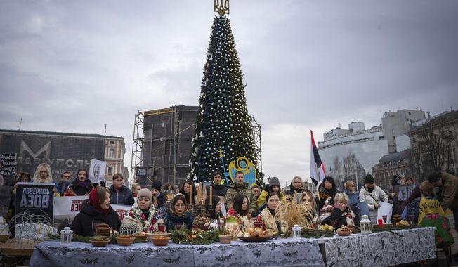 Relatives of soldiers from the Azov Regiment, who were captured by Russia in May after the fall of Mariupol, sit at the Christmas table in a flashmob action under the Christmas tree demanding to free the prisoners, in Kyiv, Ukraine, Saturday, Dec. 24, 2022. (AP Photo/Efrem Lukatsky)