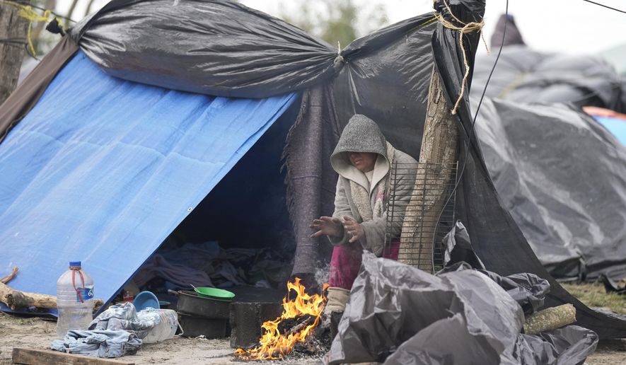 A Venezuelan migrant warms her hands over a campfire outside her makeshift tent refusing to be relocated to a refugee shelter, in Matamoros, Mexico, Friday, Dec. 23, 2022. Migrants are waiting along the U.S.-Mexico border on a pending U.S. Supreme Court decision on asylum restrictions. (AP Photo/Fernando Llano)