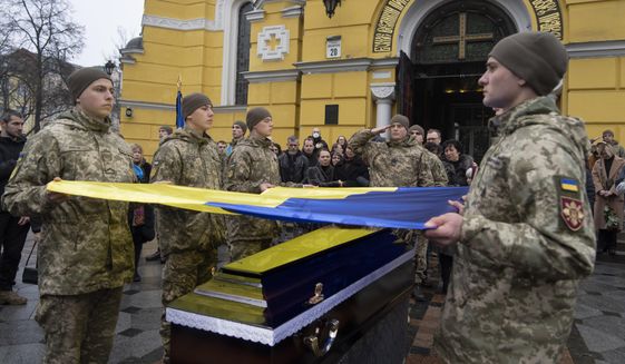 Ukrainian servicemen hold a flag over the coffin of their comrade during the funeral ceremony of Volodymyr Yezhov killed in a battlefield with Russian forces at St. Volodymyr Cathedral in Kyiv, Ukraine, Tuesday, Dec. 27, 2022. Yezhov was a game designer in the development of the game Cossacks 2. He was also one of the authors of the game S.T.A.L.K.E.R.: Clear Sky. Yezhov was also one of the most famous Ukrainian e-sportsmen — played StarCraft under the nickname Fresh. Since the Russian invasion, Volodymyr Yezhov went to the frontline and fought as part of the volunteer squadron. (AP Photo/Efrem Lukatsky)