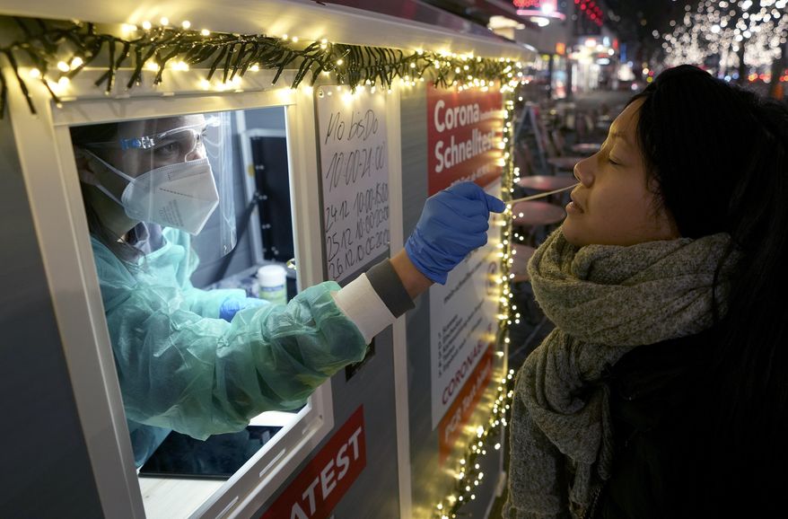 FILE -- A test center employee performs a coronavirus test as she stands in the 'Kurfuerstendamm (Ku'damm)' shopping road in Berlin, Germany, Tuesday, Dec. 21, 2021. Germany's governing coalition is arguing over whether remaining coronavirus restrictions should be dropped after one of the country's top virologists was quoted as saying that the COVID-19 pandemic is over. (AP Photo/Michael Sohn, file)