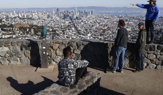 Tourists look out onto the city skyline from Christmas Tree Point on top of Twin Peaks in San Francisco, Thursday, Dec. 15, 2022. (Jessica Christian/San Francisco Chronicle via AP)