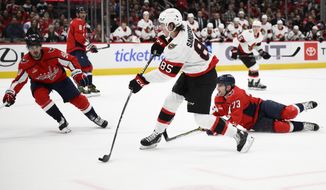 Ottawa Senators defenseman Jake Sanderson (85) shoots the puck against Washington Capitals left wing Conor Sheary (73) and left wing Marcus Johansson (90) during the second period of an NHL hockey game Thursday, Dec. 29, 2022, in Washington. (AP Photo/Nick Wass)
