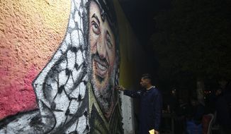 A Palestinian artist paints a portrait of of the late Palestinian president Yasser Arafat, on a wall in preparation of celebration of 58th Fatah anniversary, at the main square in Gaza City, Friday, Dec. 30, 2022. (AP Photo/Adel Hana)