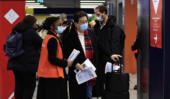Passengers arriving from China wait in front of a COVID-19 testing area set at the Roissy Charles de Gaulle airport, north of Paris, Sunday, Jan. 1, 2023. France says it will require negative COVID-19 tests of all passengers arriving from China and is urging French citizens to avoid nonessential travel to China. (AP Photo/Aurelien Morissard)