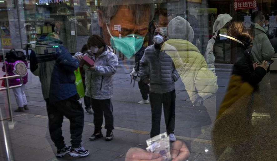 Visitors are reflected on a window pane as a man counts Chinese currency notes at a shop selling tea in Qianmen, a popular tourist spot in Beijing, Tuesday, Jan. 3, 2023. As the virus continues to rip through China, global organizations and governments have called on the country start sharing data while others have criticized its current numbers as meaningless. (AP Photo/Andy Wong)