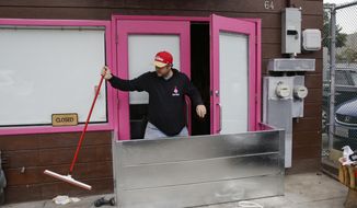 Owner Matthew Coric climbs over a metal flood gate his family members helped install in front of Pink Onion, a pizzeria in the Mission District in San Francisco on Tuesday, Jan. 3, 2023. Pink Onion saw serious flooding and damage Saturday. Coric and family members were preparing for an upcoming storm. (Salgu Wissmath/San Francisco Chronicle via AP)