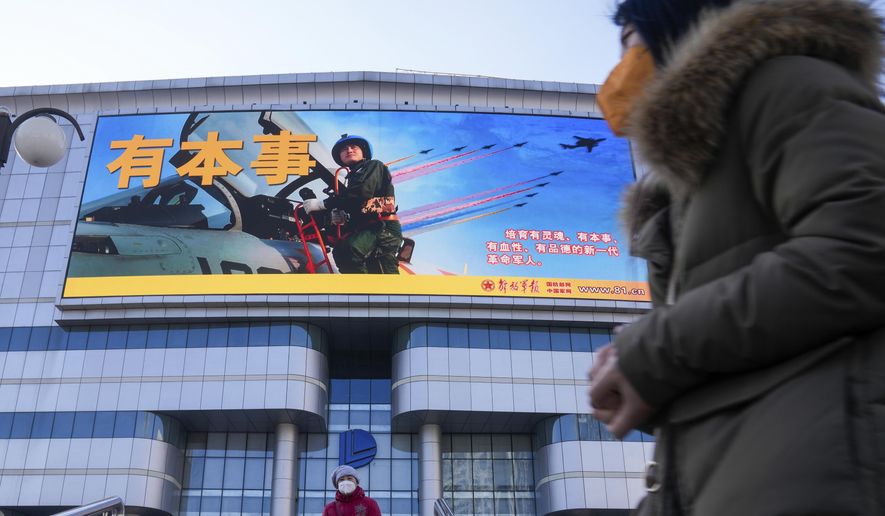 Residents wearing face masks walk by a large screen showing the Chinese People&#39;s Liberation Army Airforce outside a mall in Beijing, Monday, Jan. 9, 2023. The Chinese military held large-scale joint combat strike drills starting Sunday, sending war planes and navy vessels toward Taiwan, both the Chinese and Taiwanese defense ministries said. (AP Photo/Andy Wong)