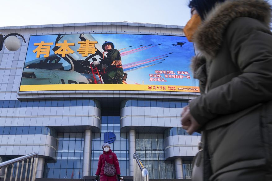 Residents wearing face masks walk by a large screen showing the Chinese People&#x27;s Liberation Army Airforce outside a mall in Beijing, Monday, Jan. 9, 2023. The Chinese military held large-scale joint combat strike drills starting Sunday, sending war planes and navy vessels toward Taiwan, both the Chinese and Taiwanese defense ministries said. (AP Photo/Andy Wong)