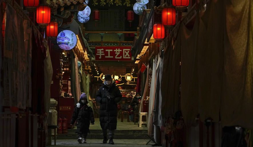 A man and a child wearing face masks walk by shuttered stores on Jan. 3, 2023, which would be selling souvenirs in Qianmen, a popular tourist spot in Beijing. China’s business and consumer activity might revive as early as the first quarter of this year, but before that happens, entrepreneurs and families face a painful squeeze from a surge in cases that has left employers without enough healthy workers and kept wary customers away from shopping malls, restaurants, hair salons and gyms. (AP Photo/Andy Wong)