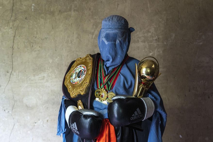 Afghan mixed martial arts fighter poses for a photo with her trophies in Kabul, Afghanistan, Monday, Oct. 31, 2022. The ruling Taliban have banned women from sports as well as barring them from most schooling and many realms of work. A number of women posed for an AP photographer for portraits with the equipment of the sports they loved. Though they do not necessarily wear the burqa in regular life, they chose to hide their identities with their burqas because they fear Taliban reprisals and because some of them continue to practice their sports in secret. (AP Photo/Ebrahim Noroozi)