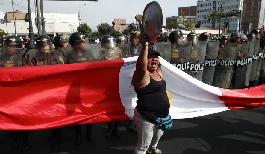 An anti-government protester stand in front of police blocking a march against President Dina Boluarte in Lima, Peru, Thursday, Jan. 19, 2023. Protesters are seeking immediate elections, the resignation of Boluarte, the release from prison of ousted President Pedro Castillo and justice for protesters killed in clashes with police. (AP Photo/Hugo Curotto)