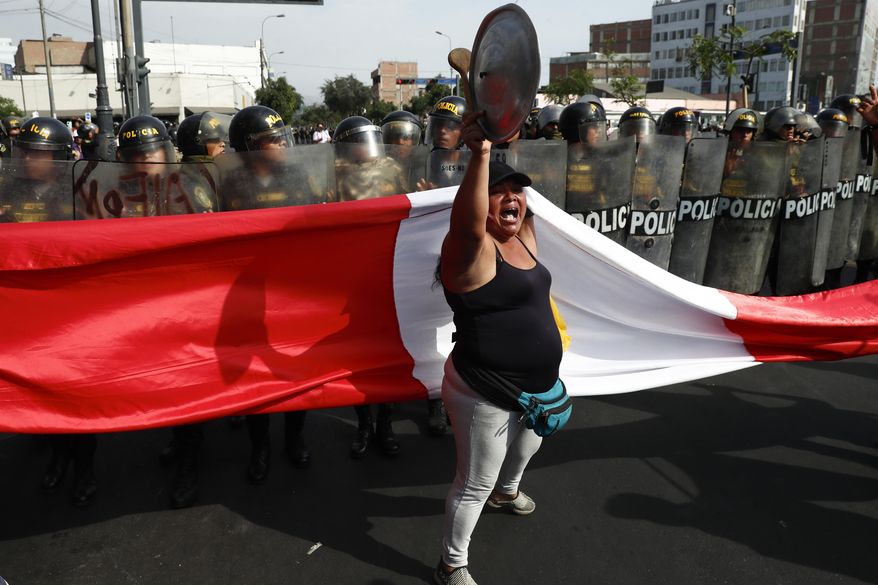An anti-government protester stand in front of police blocking a march against President Dina Boluarte in Lima, Peru, Thursday, Jan. 19, 2023. Protesters are seeking immediate elections, the resignation of Boluarte, the release from prison of ousted President Pedro Castillo and justice for protesters killed in clashes with police. (AP Photo/Hugo Curotto)
