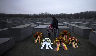 A father with his two kids stay behine wreaths, placed at the Memorial to the Murdered Jews of Europe on the International Holocaust Remembrance Day in Berlin, Germany, Friday, Jan. 27, 2023. (AP Photo/Markus Schreiber)