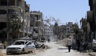 FILE - Syrians walk through destruction in the town of Douma, the site of a suspected chemical weapons attack, near Damascus, Syria, Monday, April 16, 2018. A report published Friday, Jan. 27, 2023, by a team from the Organization for the Prohibition of Chemical Weapons established there are “reasonable grounds to believe” Syria&#39;s air force dropped two cylinders containing chlorine gas on the city of Douma in April 2018, killing 43 people. (AP Photo/Hassan Ammar, File)