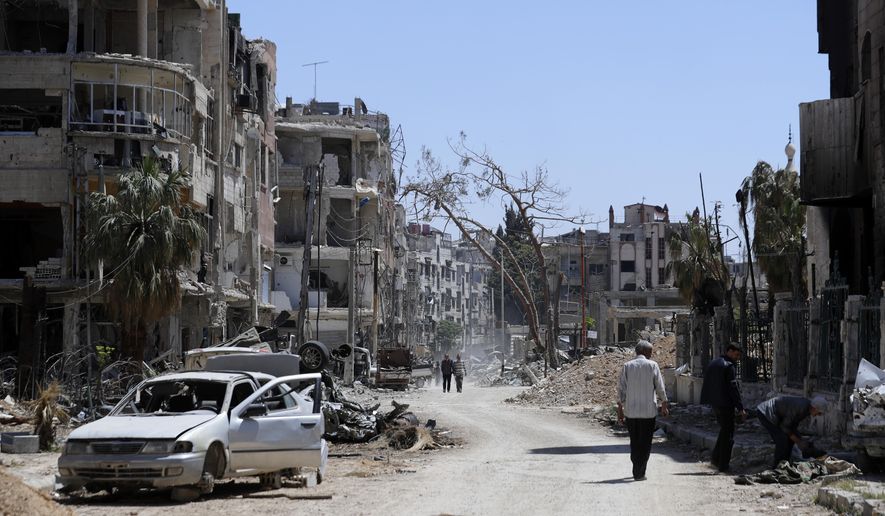 FILE - Syrians walk through destruction in the town of Douma, the site of a suspected chemical weapons attack, near Damascus, Syria, Monday, April 16, 2018. A report published Friday, Jan. 27, 2023, by a team from the Organization for the Prohibition of Chemical Weapons established there are “reasonable grounds to believe” Syria&#x27;s air force dropped two cylinders containing chlorine gas on the city of Douma in April 2018, killing 43 people. (AP Photo/Hassan Ammar, File)