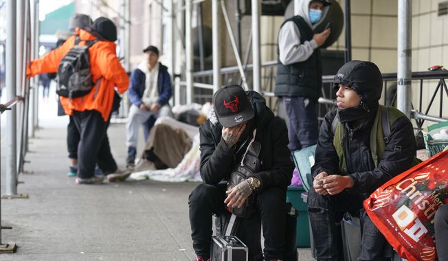 Recent immigrants to the United States sit with their belongings on the sidewalk in front of the Watson Hotel in New York, Monday, Jan. 30, 2023. The immigrants, mostly from Venezuela and other Latin American countries, had been living in the hotel until recently, when they were told to leave the temporary shelter. (AP Photo/Seth Wenig)