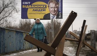 A woman passes by a board depicting former British Prime Minister Boris Johnson and reads: &quot;The World of Brave People! #thank you for support&quot;, with antitank hedgehogs in the foreground, in the town of Bucha, outside Kyiv, Ukraine, Monday Jan. 30, 2023. (AP Photo/Efrem Lukatsky)