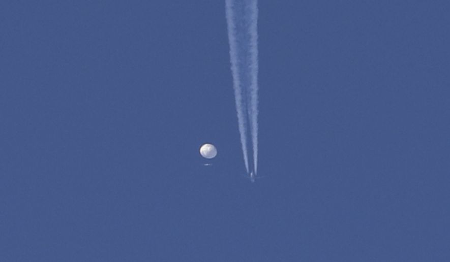 In this photo provided by Brian Branch, a large balloon drifts above the Kingston, N.C. area, with an airplane and its contrail seen below it. The United States says it is a Chinese spy balloon moving east over America at an altitude of about 60,000 feet (18,600 meters), but China insists the balloon is just an errant civilian airship used mainly for meteorological research that went off course due to winds and has only limited “self-steering” capabilities. (Brian Branch via AP)