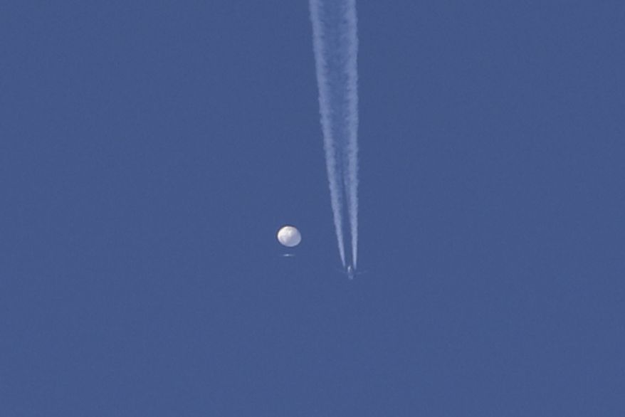In this photo provided by Brian Branch, a large balloon drifts above the Kingston, N.C. area, with an airplane and its contrail seen below it. The United States says it is a Chinese spy balloon moving east over America at an altitude of about 60,000 feet (18,600 meters), but China insists the balloon is just an errant civilian airship used mainly for meteorological research that went off course due to winds and has only limited “self-steering” capabilities. (Brian Branch via AP)
