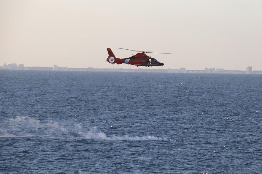 In this image provided by the U.S. Navy, a U.S. Coast Guard helicopter flies over a debris field during recovery efforts of a high-altitude surveillance balloon, Saturday, Feb. 4, 2023, off the coast of South Carolina. A U.S. Coast Guard helicopter crew (not pictured) airlifted a Florida man from a life raft off Puerto Rico and flew him to safety this weekend after he had fled his boat from fear that the larger vessel would capsize. (Jerry Ireland/U.S. Navy via AP)