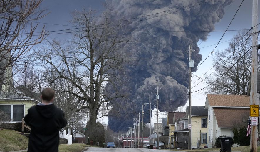 A man takes photos as a black plume rises over East Palestine, Ohio, as a result of a controlled detonation of a portion of the derailed Norfolk Southern train, Feb. 6, 2023. After toxic chemicals were released into the air from a wrecked train in Ohio, evacuated residents remain in the dark about what toxic substances are lingering in their vacated neighborhoods while they await approval to return home. (AP Photo/Gene J. Puskar, File)