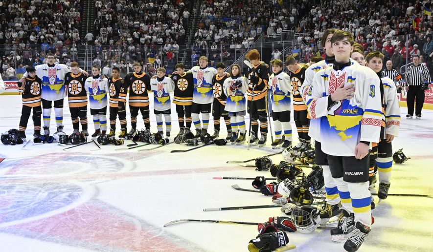 Ukraine and Boston Junior Bruins peewee teams stand together during the national anthems before a hockey game, Saturday, Feb, 11, 2023, in Quebec City. (Jacques Boissinot/The Canadian Press via AP)