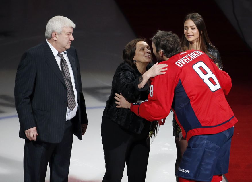 FILE - Mikhail Ovechkin, stands as his wife receives a kiss from their son, Washington Capitals left wing Alex Ovechkin, with his then-fiancé Nastya Shubskay, right, before he was presented a commemorative hockey stick by owner Ted Leonsis, Jan. 14, 2016, in Washington. Ovechkin says his father, Mikhail, has died. The Capitals captain delivered the news in Russian on his Instagram account. Ovechkin left the team yesterday to tend to a family health matter regarding a loved one. Coach Peter Laviolette said he expected Ovechkin to be gone for at least the rest of the week and away for the foreseeable future. (AP Photo/Alex Brandon, file)