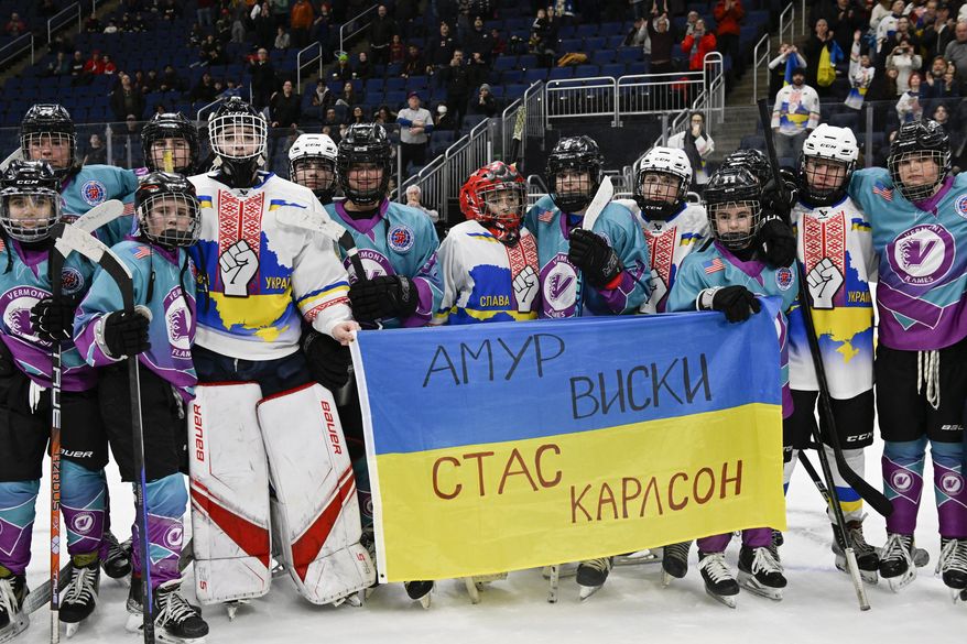 Vermont Flames Academy and Ukraine hockey players stand together after a game at the International Peewee Tournament in Quebec City, Friday, Feb. 17, 2023. Ukraine lost 2-1 to Vermont Flames Academy. Written on the top of the flag is the name of Amur Whiskey, who died in the war and was the father of one of the players on the team. The bottom of the flag has the name Stas Karlson, who is the father of another player and is still fighting.(Jacques Boissinot/The Canadian Press via AP)